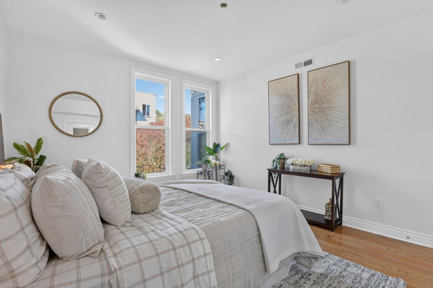 Bright bedroom with a large plaid-dressed bed, tall windows, and framed wall art.