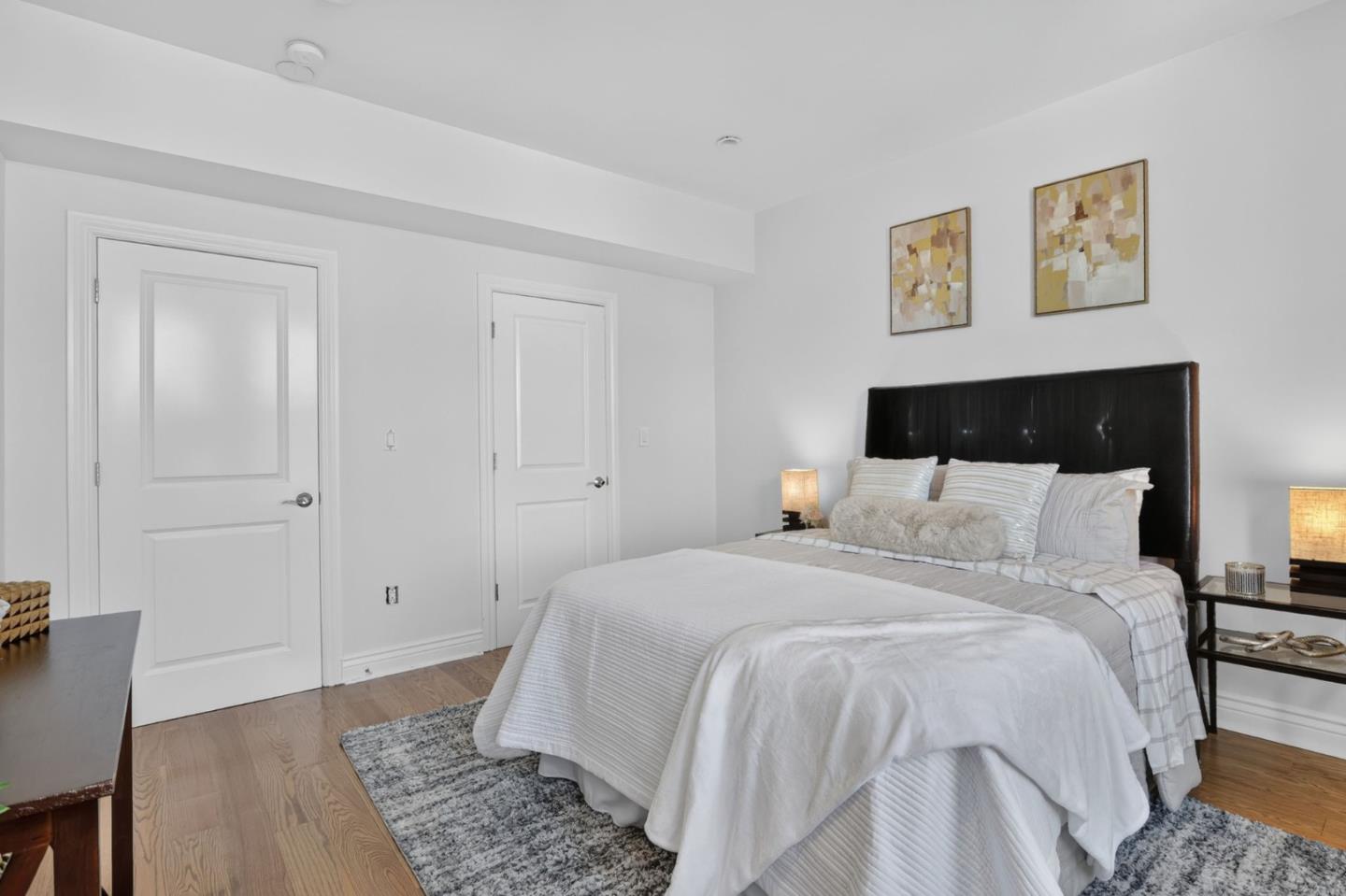 Staged bedroom with a white-covered bed, black headboard, and abstract art above it.