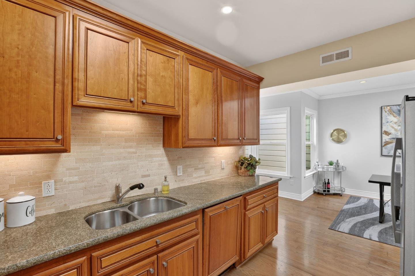 Kitchen with warm wood cabinets, stone counters, and a double-basin sink opening to a living area.