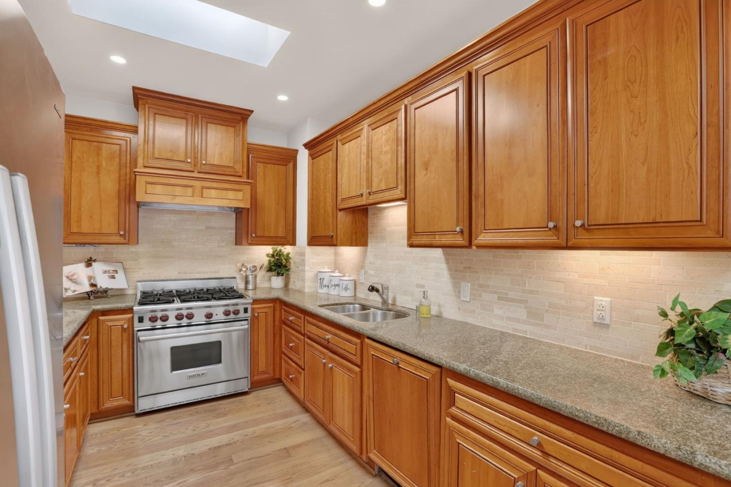 Kitchen with honey-toned wood cabinets, granite counters, gas range, and skylight.
