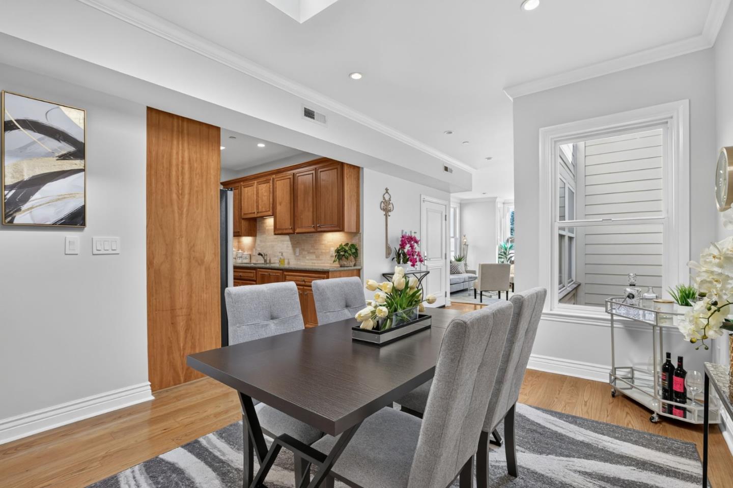 Dining room with a dark table, gray chairs, striped rug, and open kitchen with wood cabinets.
