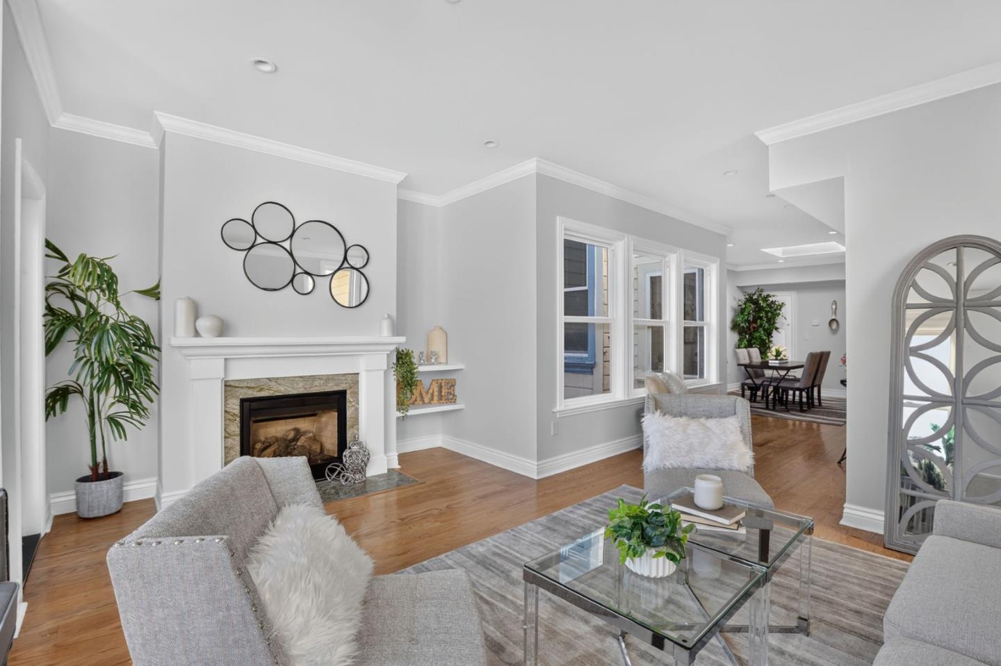 Staged living room with a white fireplace, gray seating, and an adjoining dining area.