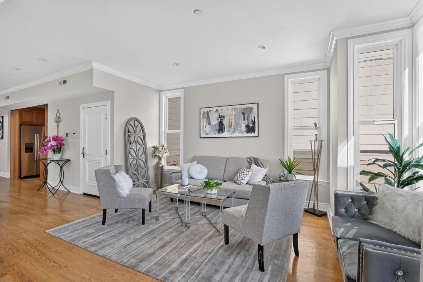 Staged living room with gray seating, a glass coffee table, striped rug, and tall windows.