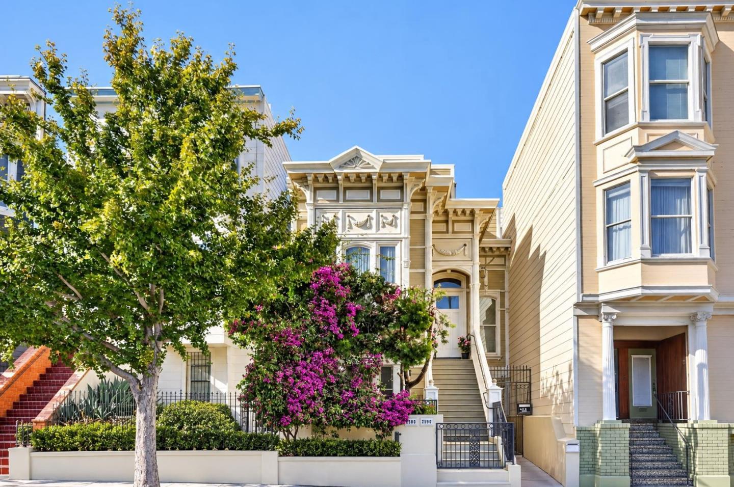 Cream Victorian home with ornate trim, front stairs, and purple bougainvillea.