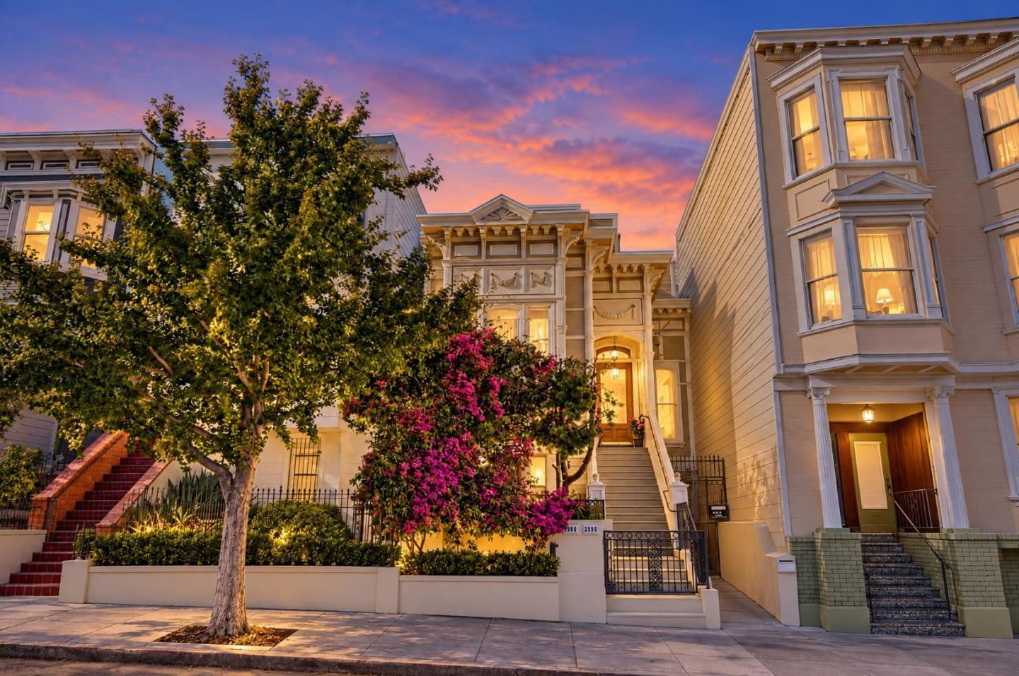 Victorian-style San Francisco homes with illuminated bay windows and flowering shrubs at dusk.