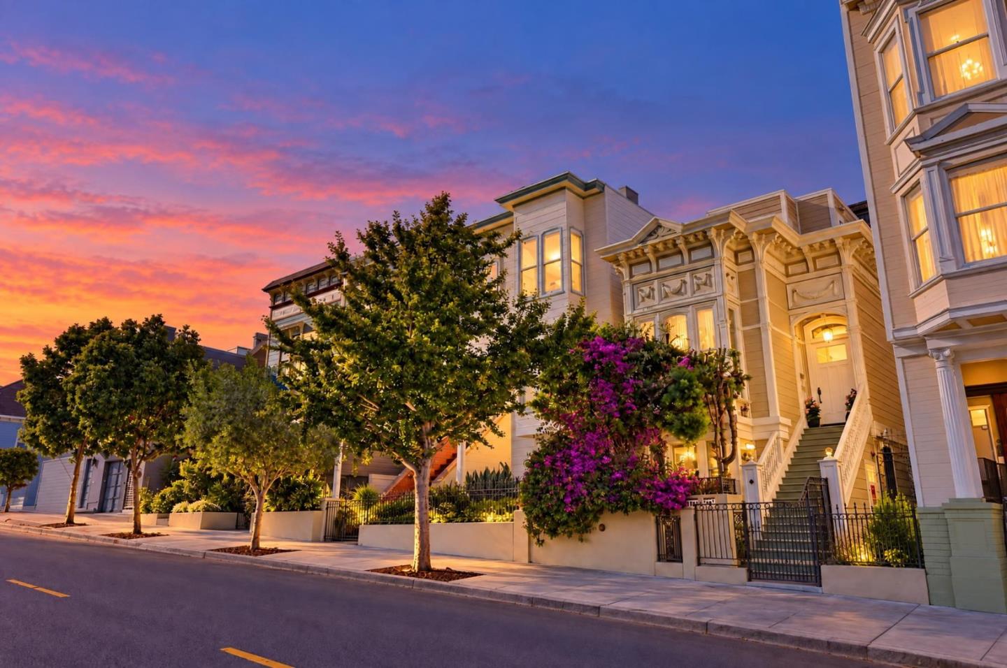 Ornate San Francisco homes with lit windows and flowering shrubs at sunset.
