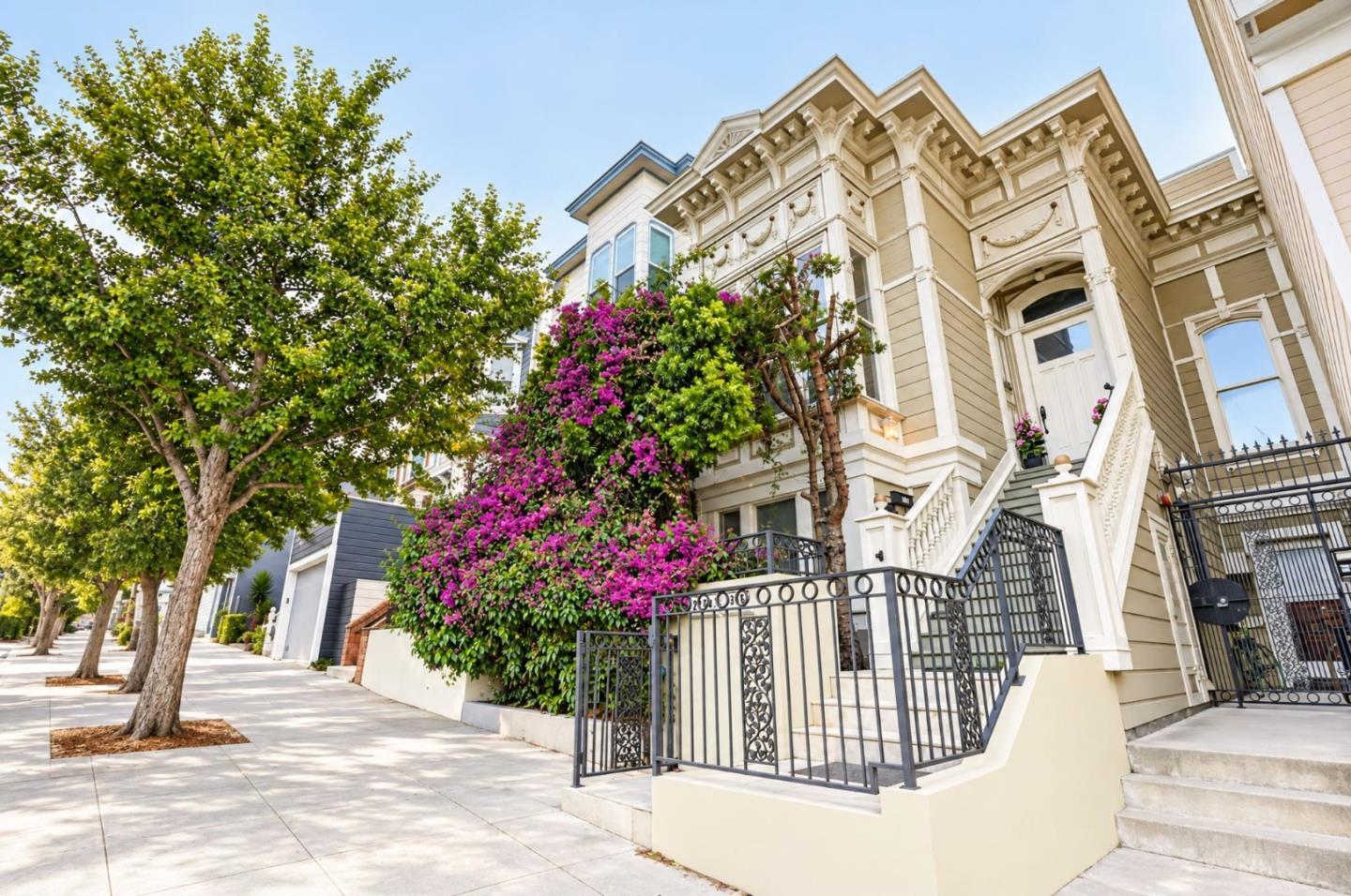 Ornate Victorian home with raised entry stairs, iron railings, and flowering shrubs.