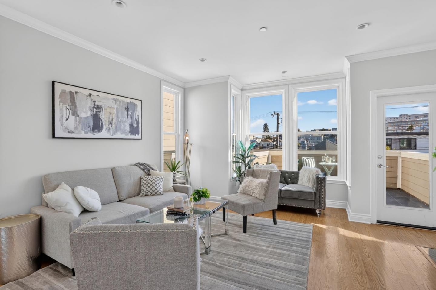 Living room with gray seating, hardwood floors, and large windows opening onto a terrace.