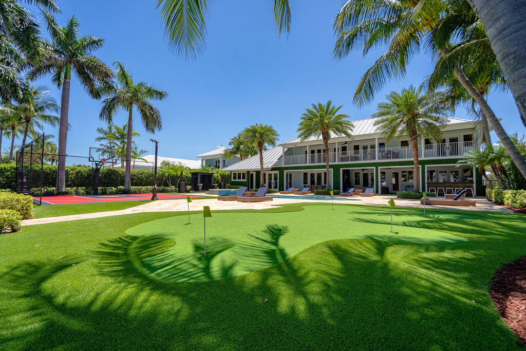 Residential courtyard with a putting green, fenced basketball court, palm trees, and outdoor seating.