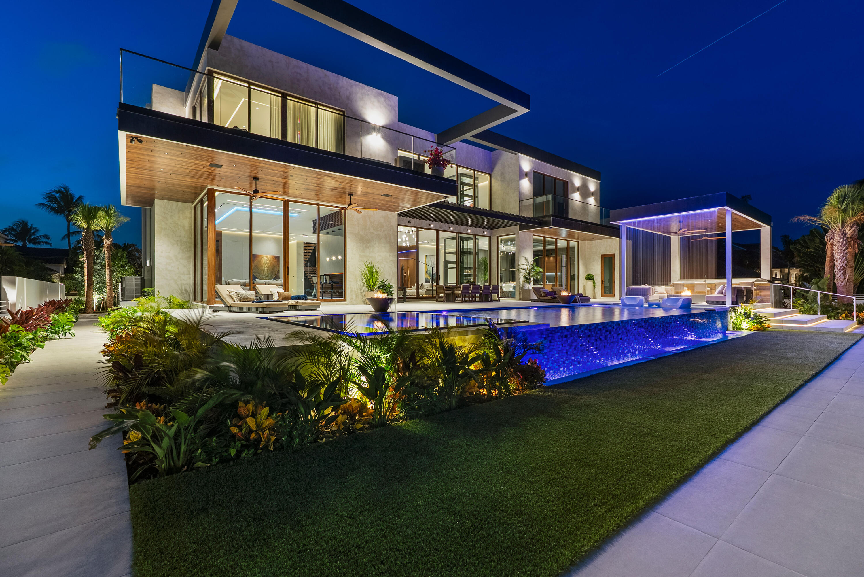 Modern two-story home with glass walls and a blue-lit pool at night.
