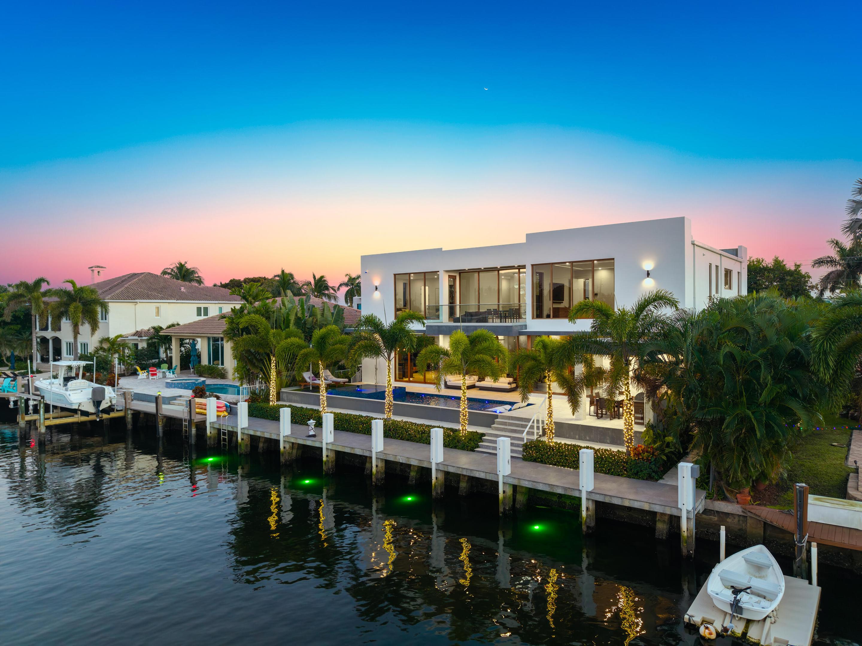 Modern waterfront home with a pool and private dock, viewed across the canal at sunset.