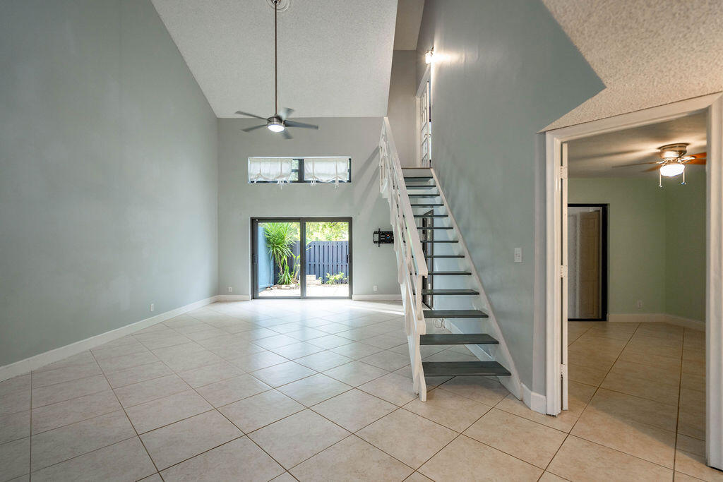 Unfurnished living room with a vaulted ceiling, open staircase, and sliding glass doors to a patio.