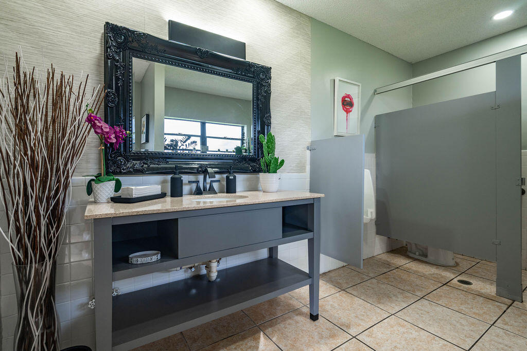 Bathroom with a gray open-shelf vanity, ornate black mirror, and tiled floor.