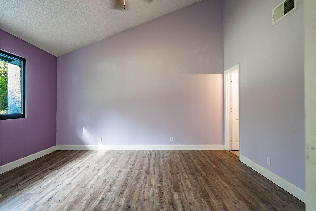 Empty room with purple walls, wood-look flooring, and a window overlooking greenery.