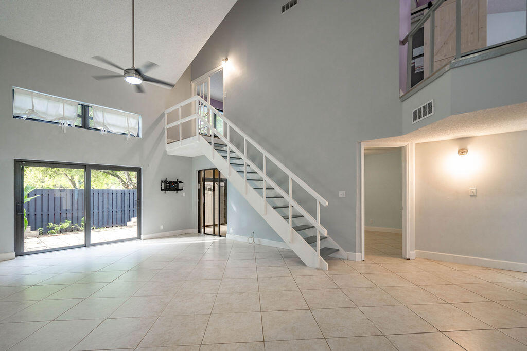 Two-story living room with a white staircase, open loft, tiled floor, and sliding doors to a fenced patio.