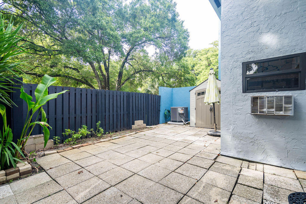 Paved patio with a dark privacy fence, tropical plants, and a small storage shed.