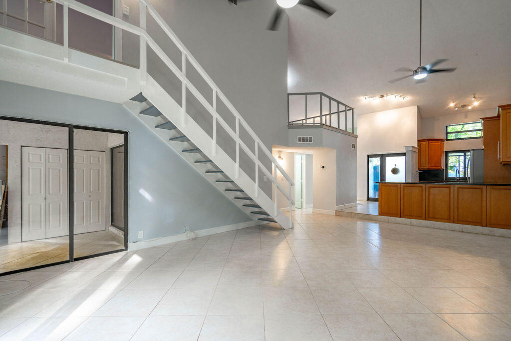 Open-plan living area with a white staircase, loft railing, tiled floors, and wood-cabinet kitchen.