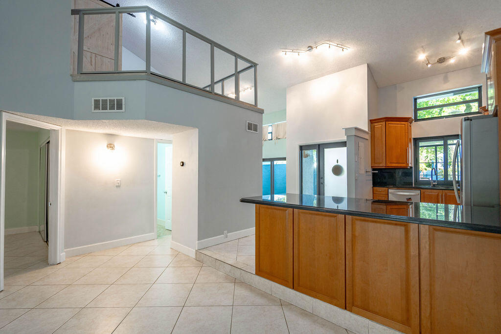 Kitchen with a long breakfast bar, wood cabinetry, tiled floors, and an open loft above.