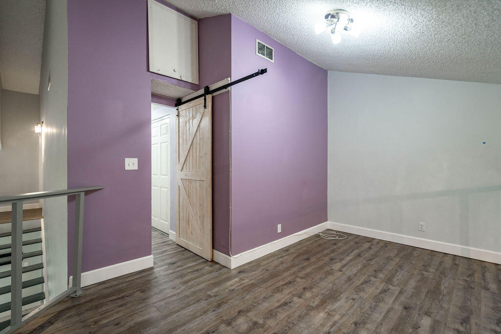 Empty room with a purple accent wall, sliding barn door, and gray wood-look flooring.