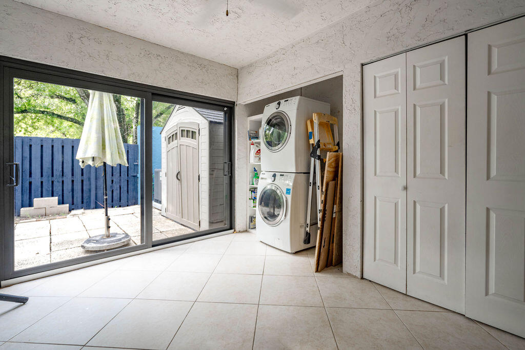 Laundry room with stacked washer and dryer beside sliding doors to a fenced patio.