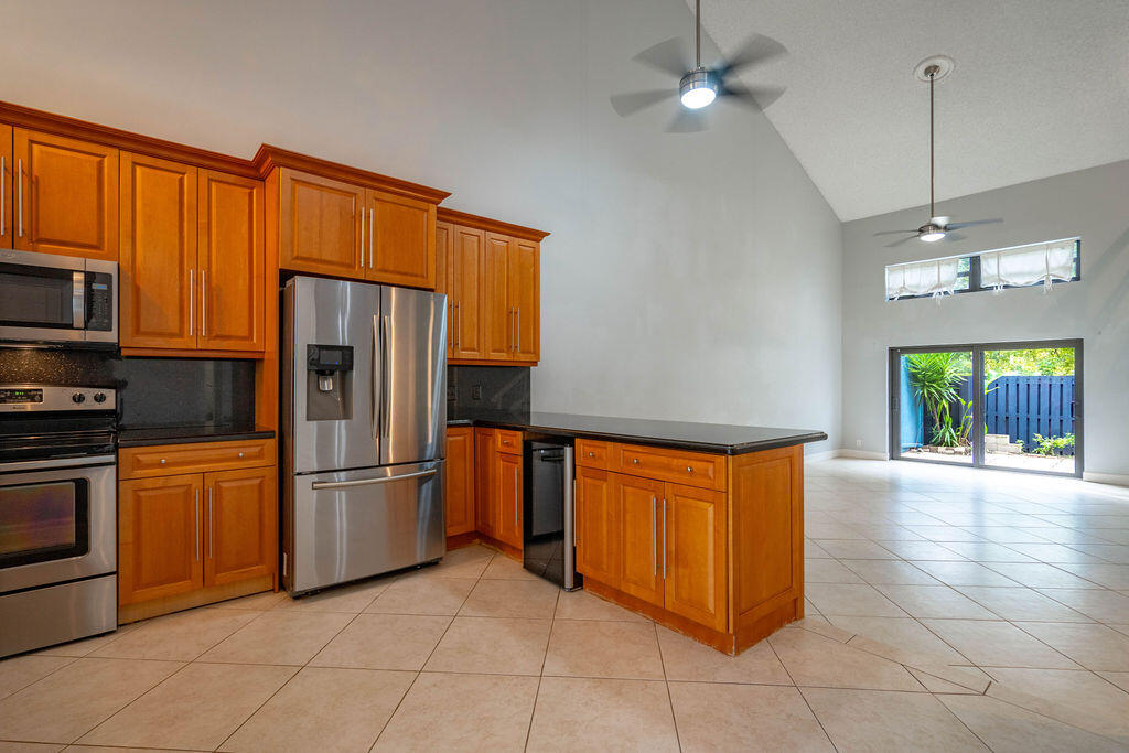 Kitchen with warm wood cabinets and stainless steel appliances, opening to a tiled living area and fenced patio.