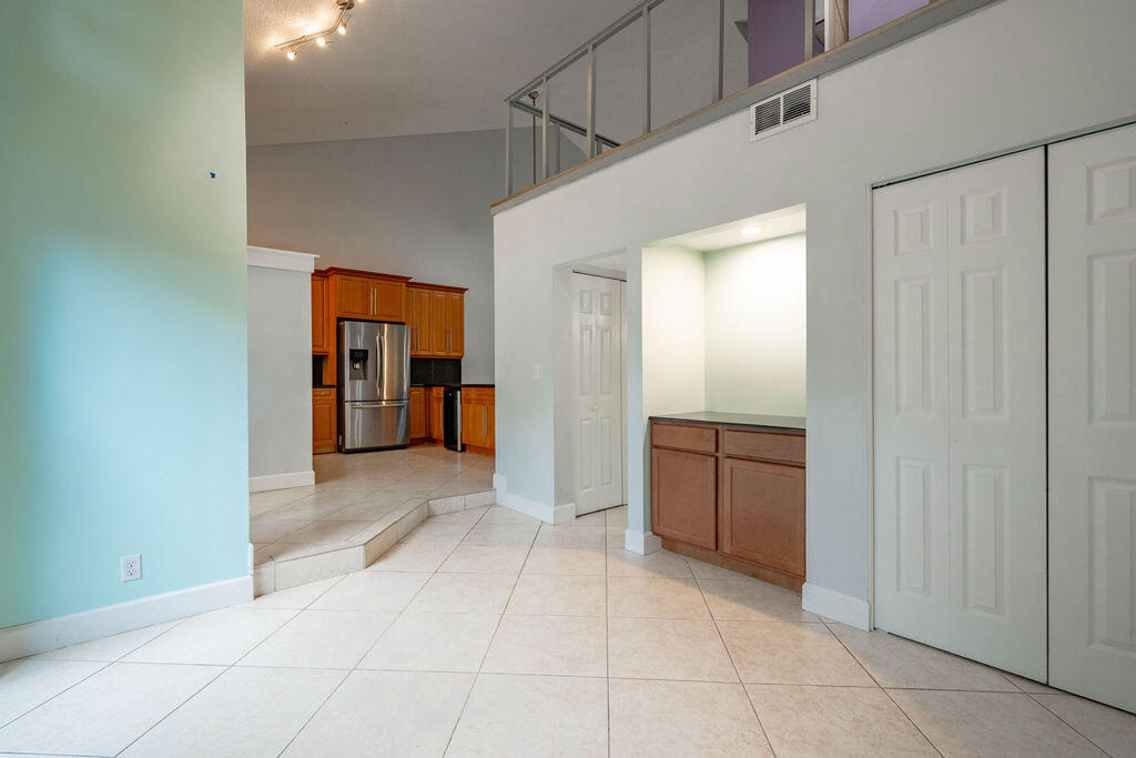 Open interior with raised kitchen, wood cabinets, stainless refrigerator, and upper-level railing.