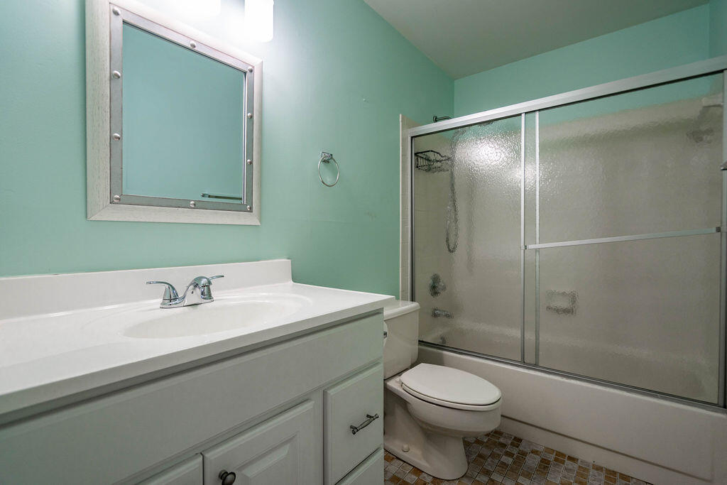 Bathroom with a white vanity, mint-green walls, and a bathtub with frosted sliding doors.