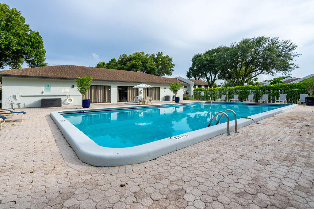 Outdoor swimming pool with metal handrails, lounge chairs, and a paved deck.