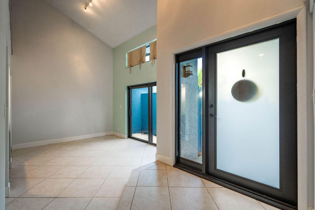 Tiled foyer with a vaulted ceiling, frosted-glass entry door, and sliding doors to a courtyard.