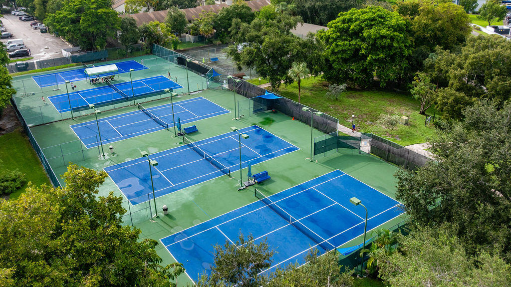 Aerial view of multiple blue tennis courts surrounded by fencing and trees.