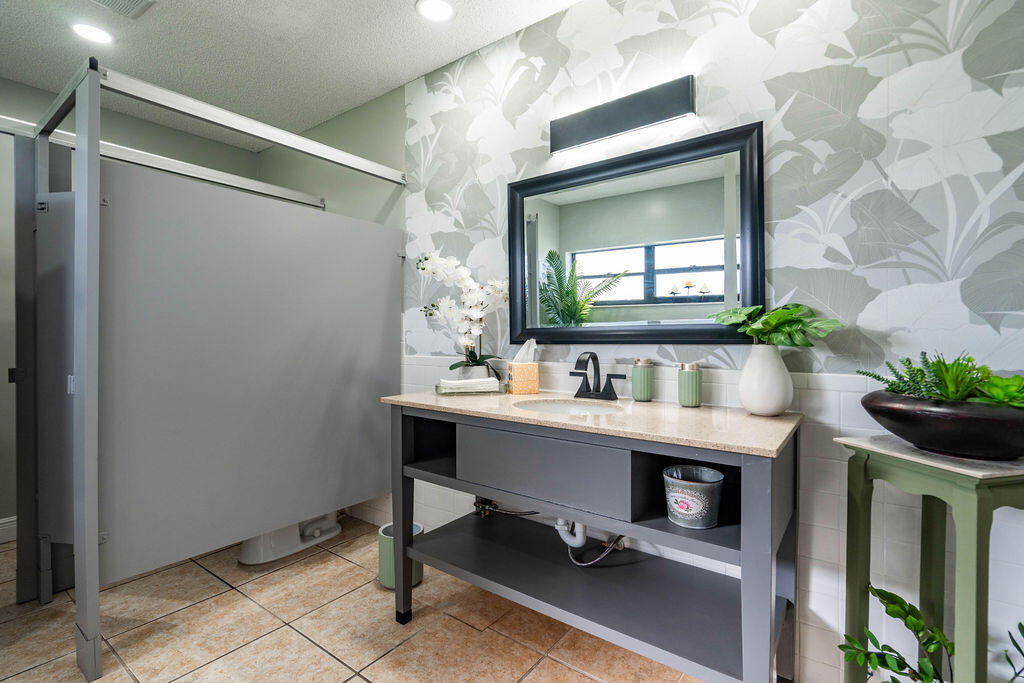 Bathroom with a gray open-shelf vanity, black faucet, leafy wallpaper, and frosted-glass shower.