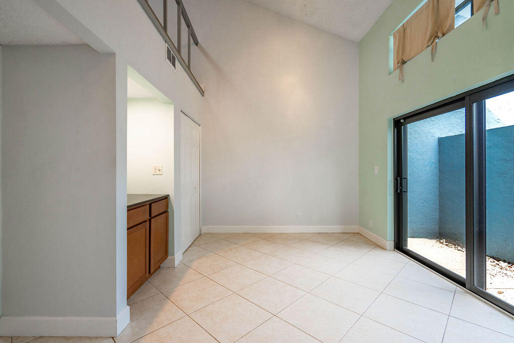 Vacant tiled room with a high ceiling and sliding glass doors to a walled outdoor area.