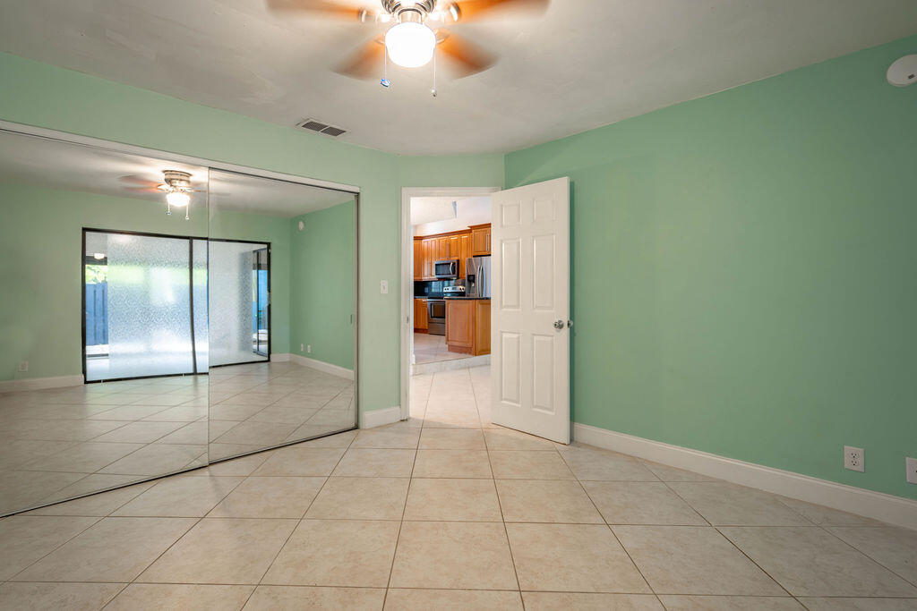Empty bedroom with mirrored closet doors, mint-green walls, and a view into the kitchen.