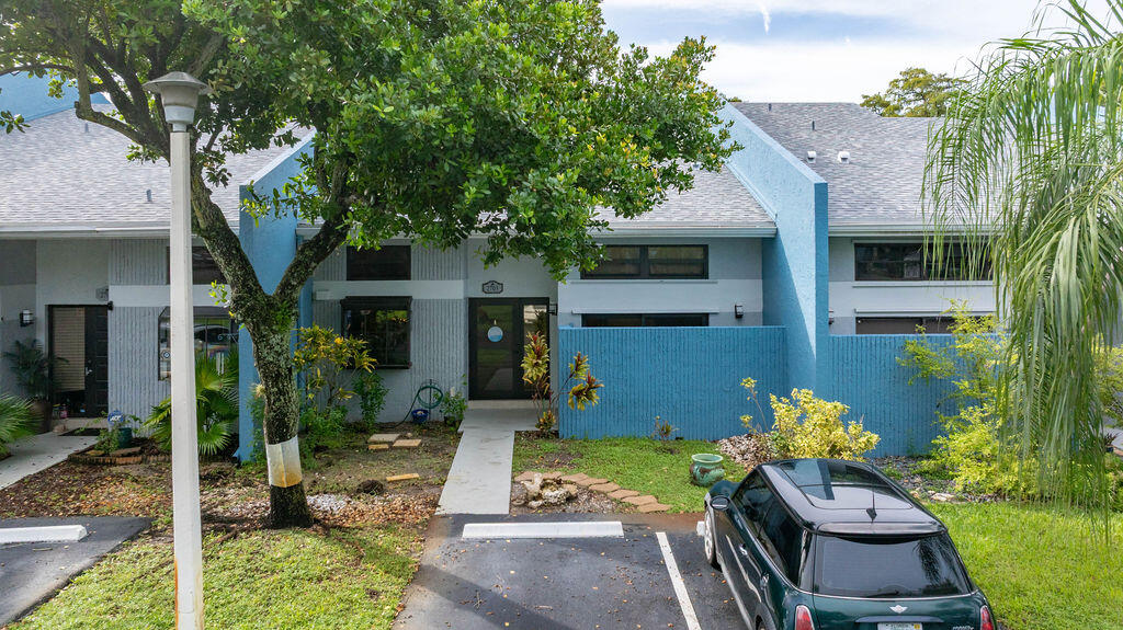 Blue attached residence with privacy walls, a front walkway, and tropical landscaping.