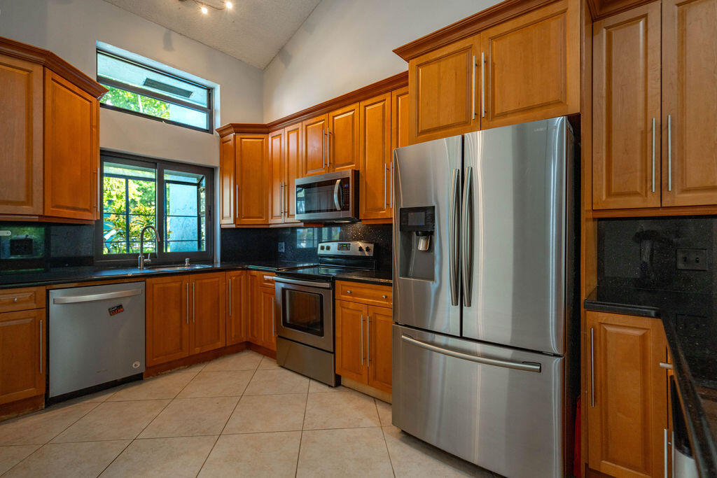 Kitchen with wood cabinets, granite counters, stainless steel appliances, and a window overlooking greenery.