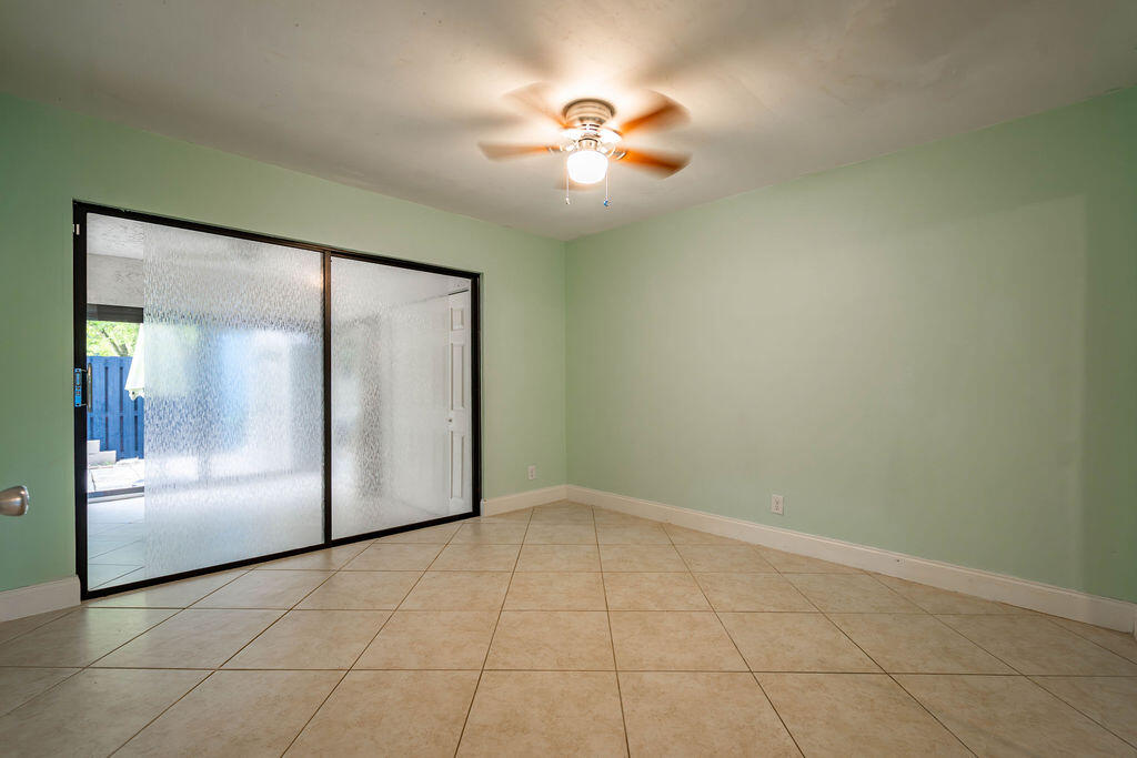 Empty pale green room with beige tile floors, a ceiling fan, and sliding glass doors.