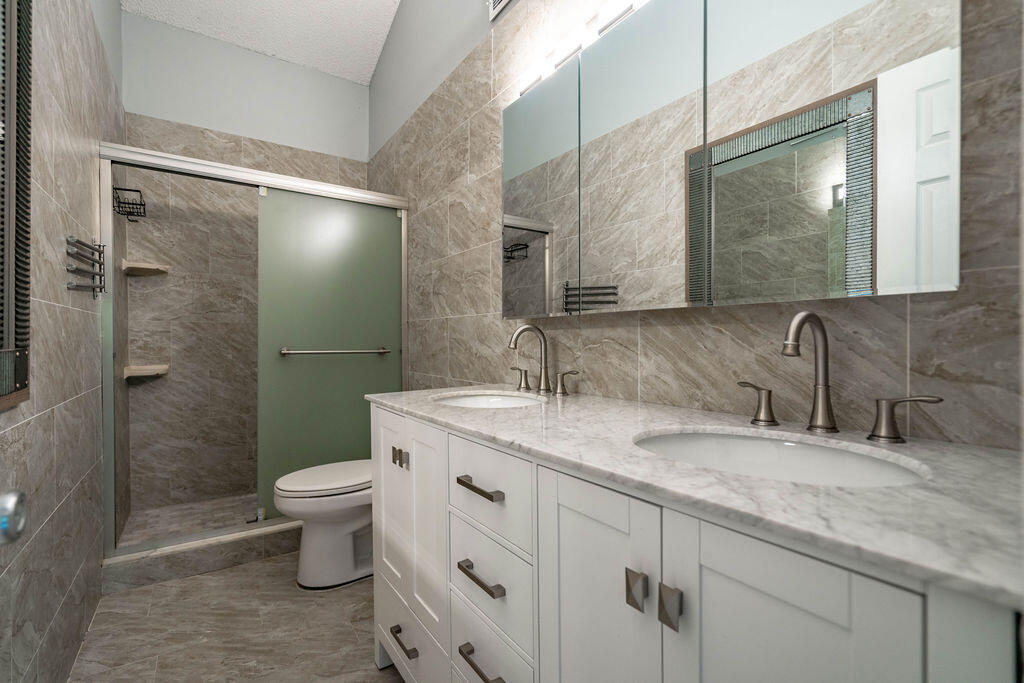 Bathroom with a long double-sink vanity, mirrored cabinets, and a glass-enclosed shower.