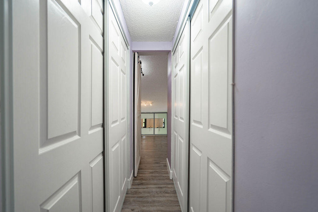 Hallway lined with white paneled closet doors, gray wood-look flooring, and pale lavender walls.