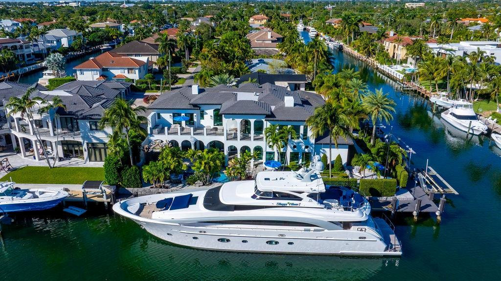 Waterfront home with a pool and dock beside a large yacht on a palm-lined canal.