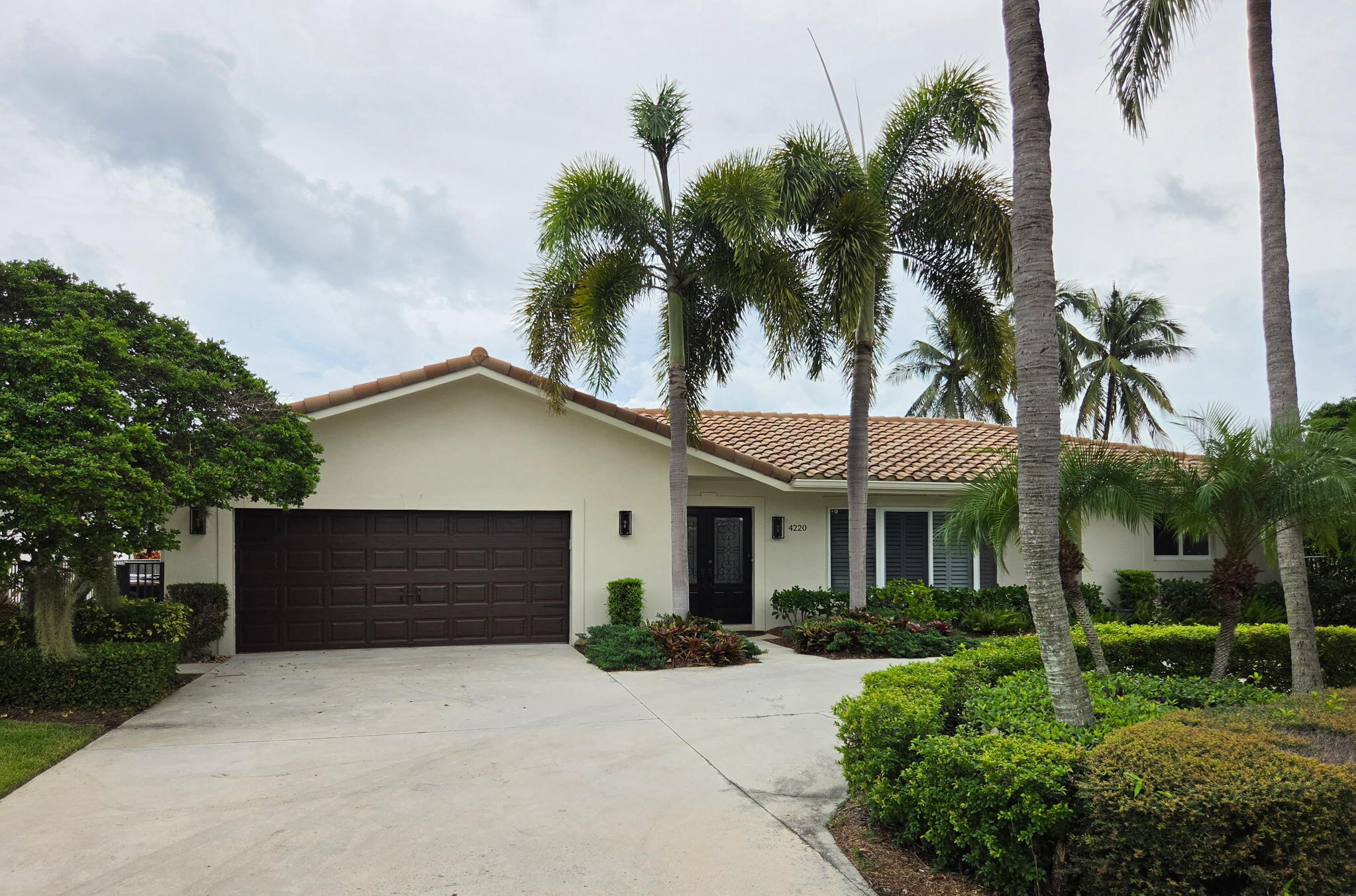 Single-story home with a tile roof, double garage, palm trees, and landscaped front yard.