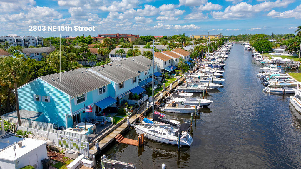 Aerial view of a turquoise waterfront home beside a canal lined with docked boats.