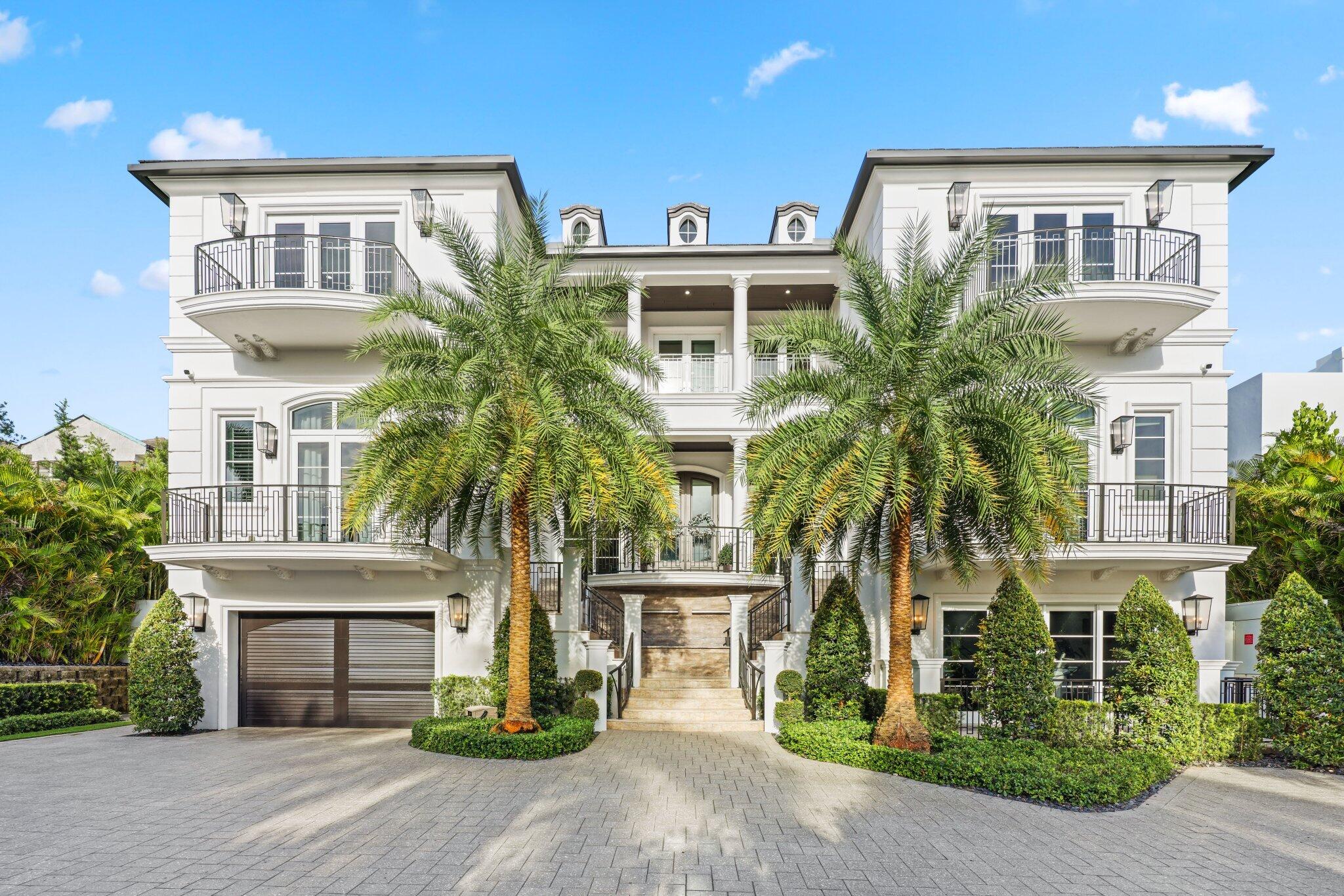 White luxury home with balconies, palm trees, and a broad paved driveway.