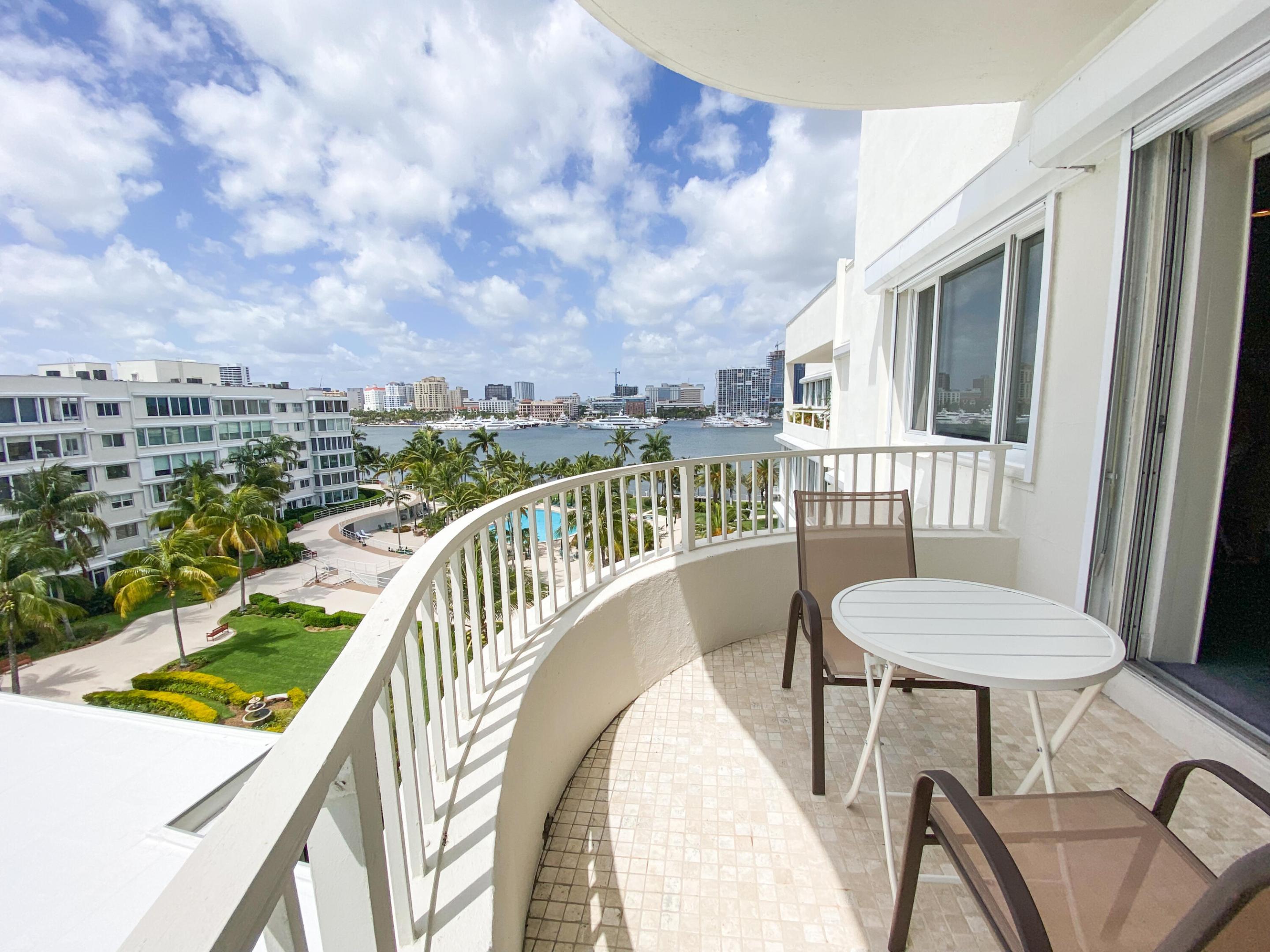 Apartment balcony overlooking palm-lined grounds, marina water, and a distant city skyline.