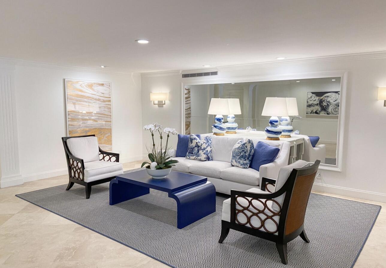 Living room with a white sofa, blue accents, sculptural navy coffee table, and large wall mirror.