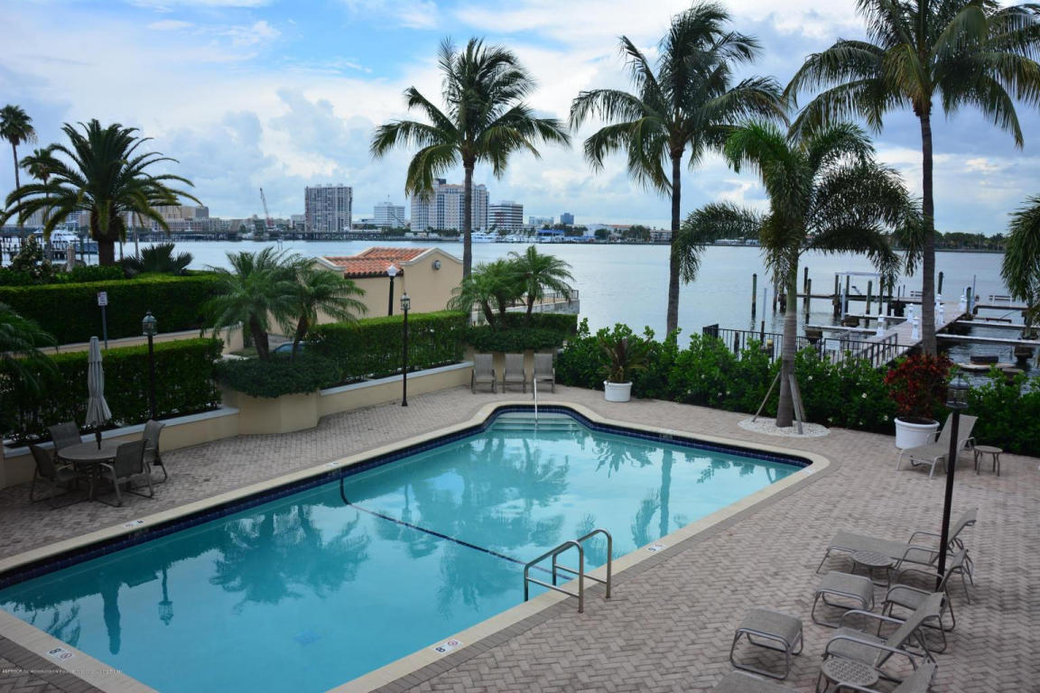Swimming pool beside a waterfront terrace with palm trees and dock.