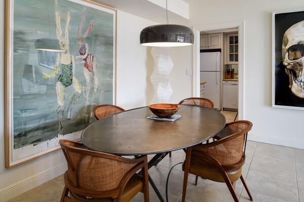 Dining room with an oval table, woven chairs, black pendant light, and large abstract artwork.