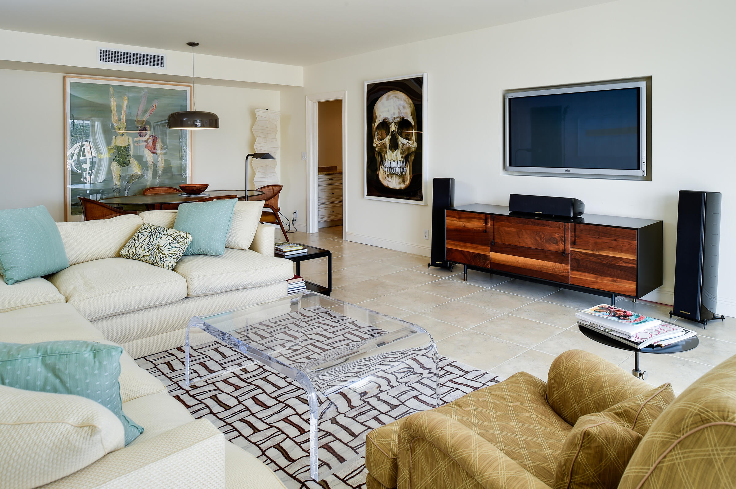 Furnished living room with cream sofas, a mustard armchair, and a clear acrylic coffee table.