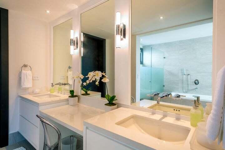 Bathroom with white double vanities, large mirrors, orchids, and a glass-enclosed bathtub and shower.