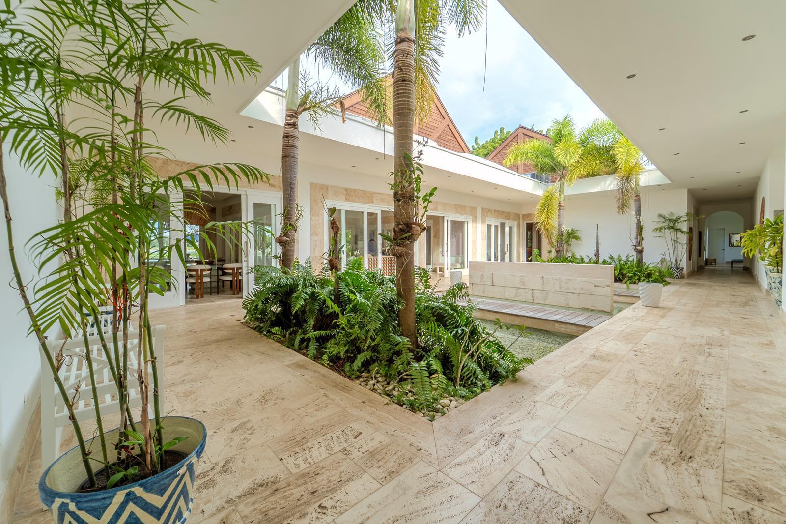 Tropical home courtyard with palm trees, a narrow reflecting pool and pale stone paving.