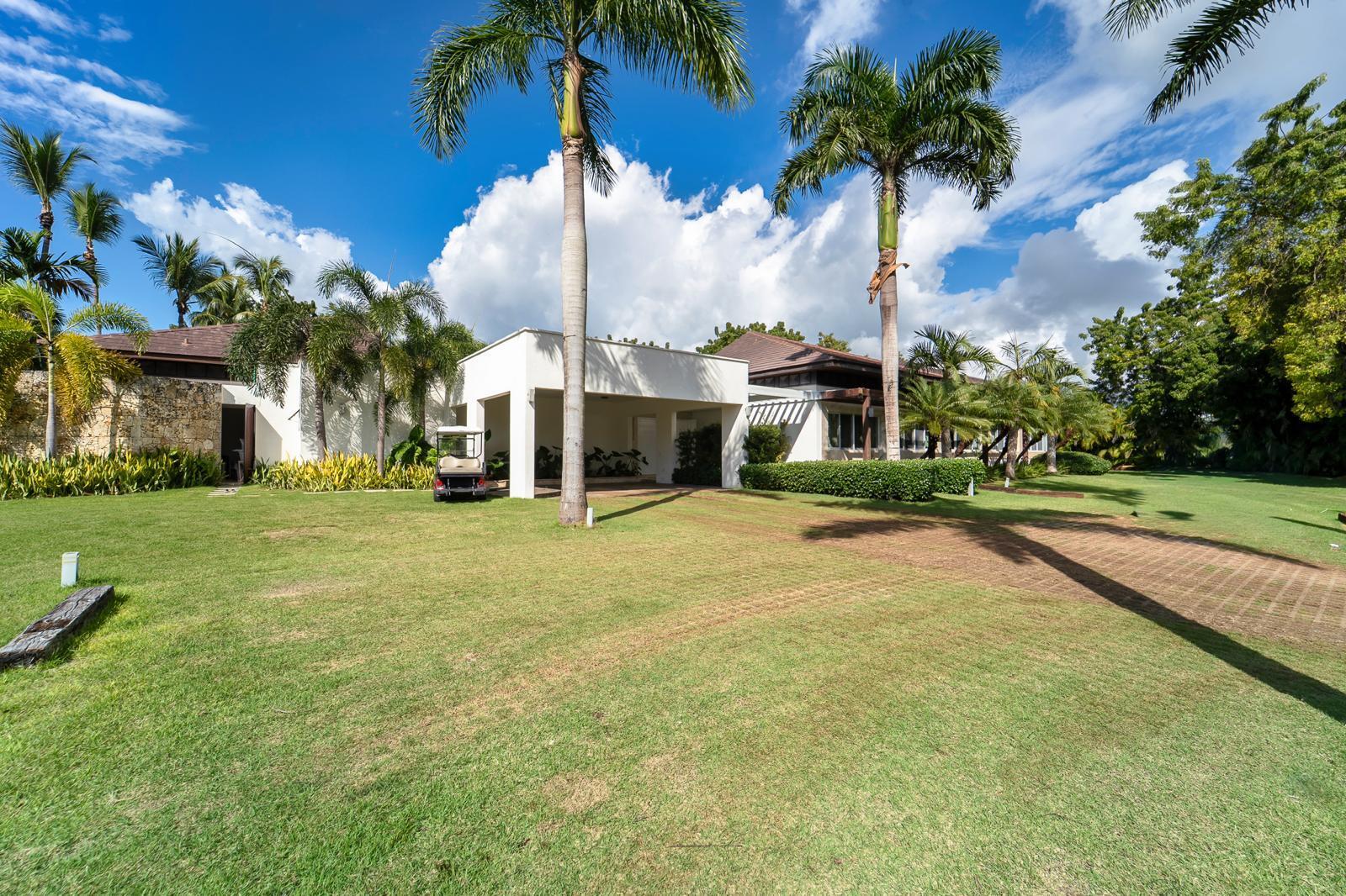Modern white home with a covered entrance, tall palms, and a broad green lawn.